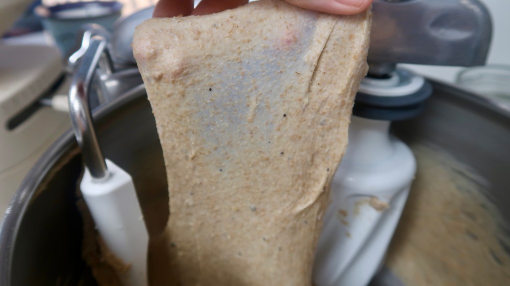 A person holding a piece of thick, creamy batter above a mixing bowl with a stand mixer, displaying its texture.