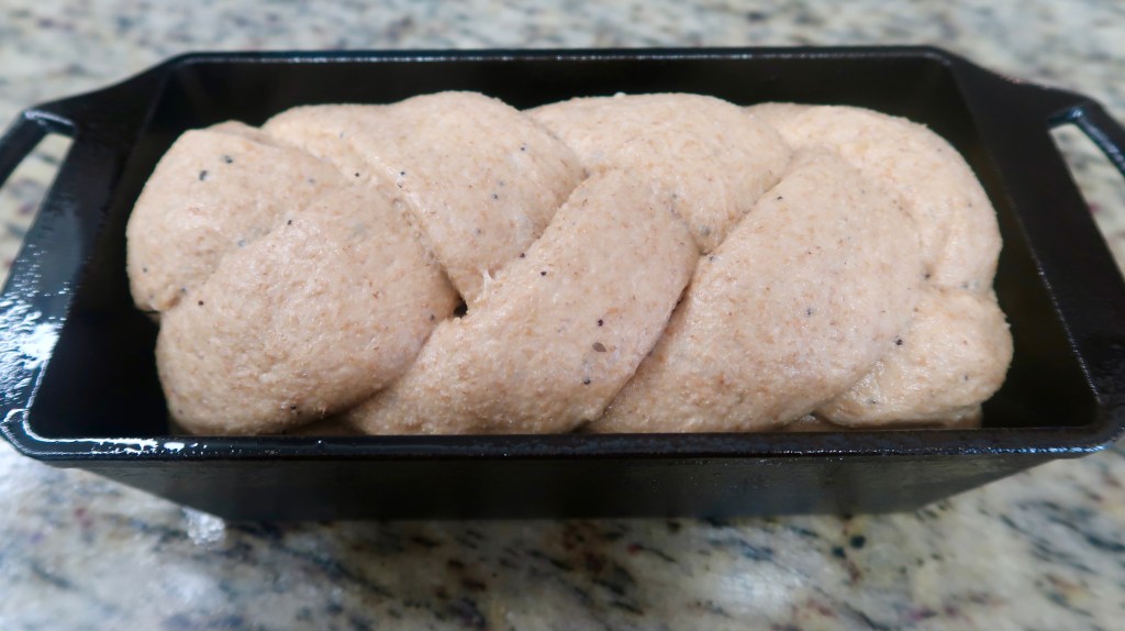A braided loaf of dough rising in a black cast iron pan on a granite countertop.