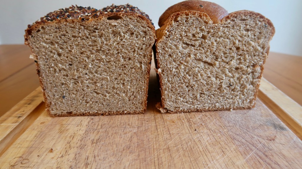 Two sliced loaves of bread on a wooden cutting board, showcasing different textures and crusts.