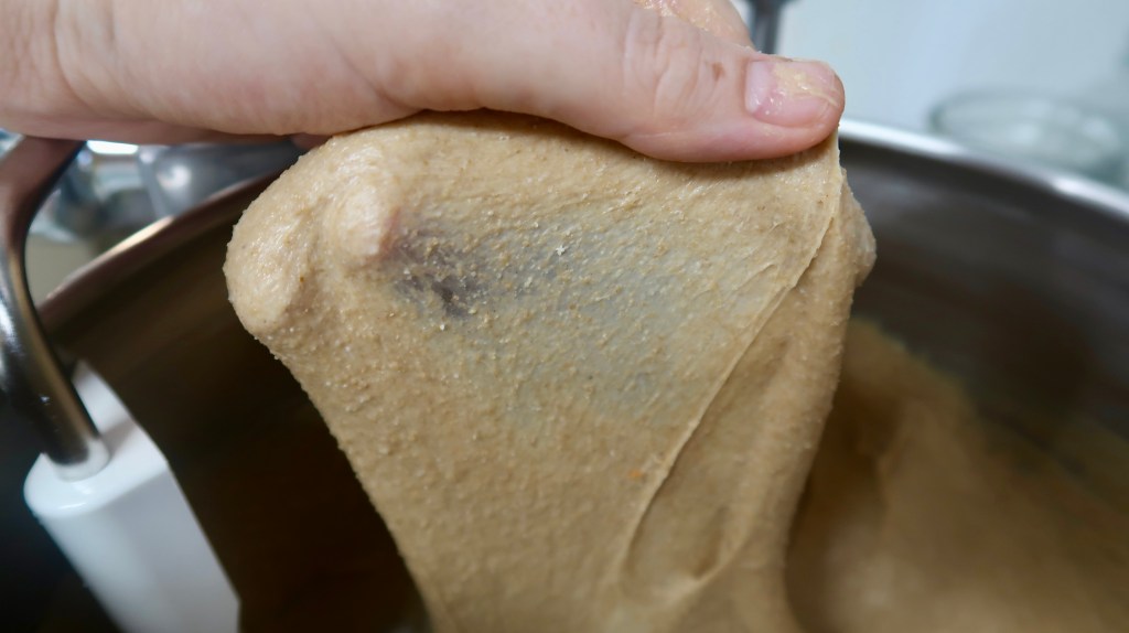 Close-up of a hand holding a thick, smooth mixture of dough or batter above a mixing bowl.