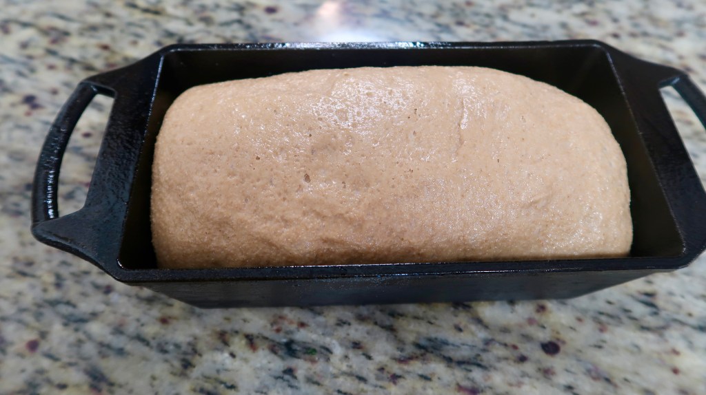 A loaf of dough rising in a black cast iron pan on a speckled countertop.