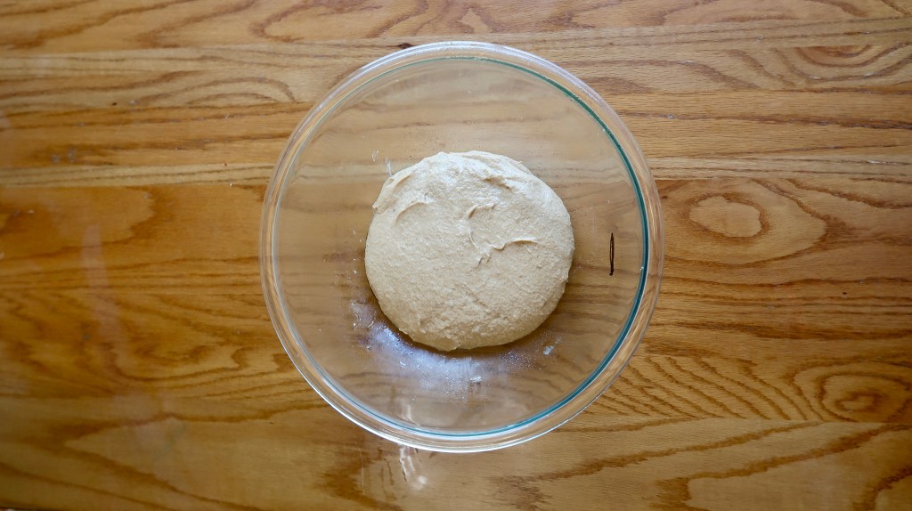 A round ball of dough resting in a clear glass bowl on a wooden countertop.