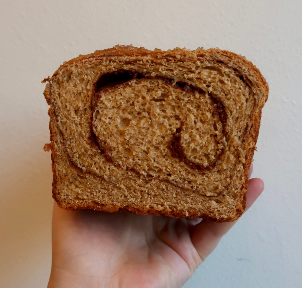 A person holding a slice of cinnamon swirl bread against a plain background.
