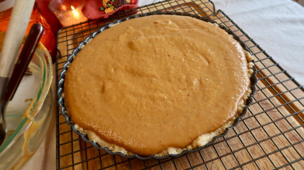 A freshly prepared pumpkin pie filling in a tart crust, cooling on a wire rack.