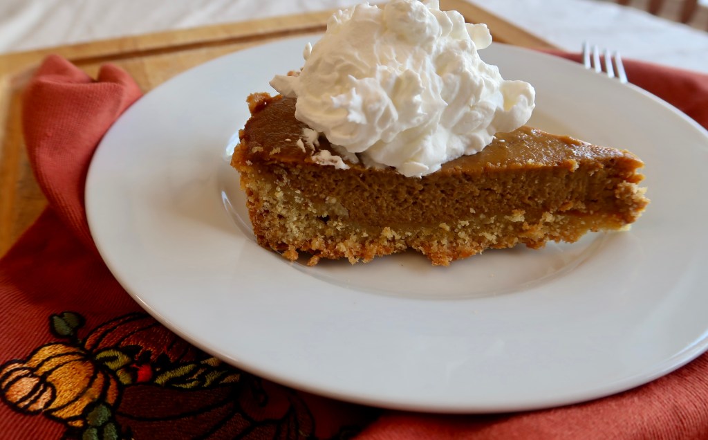 A slice of pumpkin pie topped with whipped cream, served on a white plate next to a red napkin with a pumpkin design.