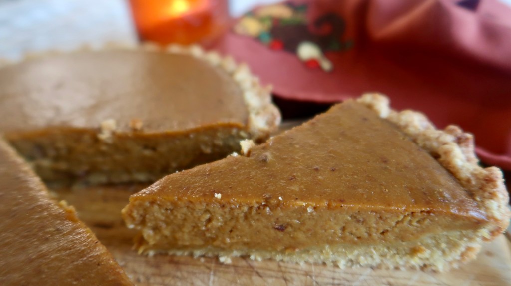 A slice of pumpkin pie on a wooden cutting board, showcasing a smooth, creamy filling and a crumbly crust, with a warm, festive background.