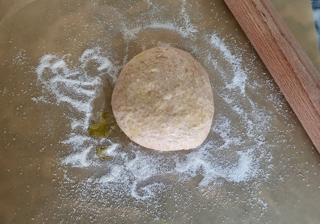 A ball of dough on a floured surface, with a wooden rolling pin beside it.