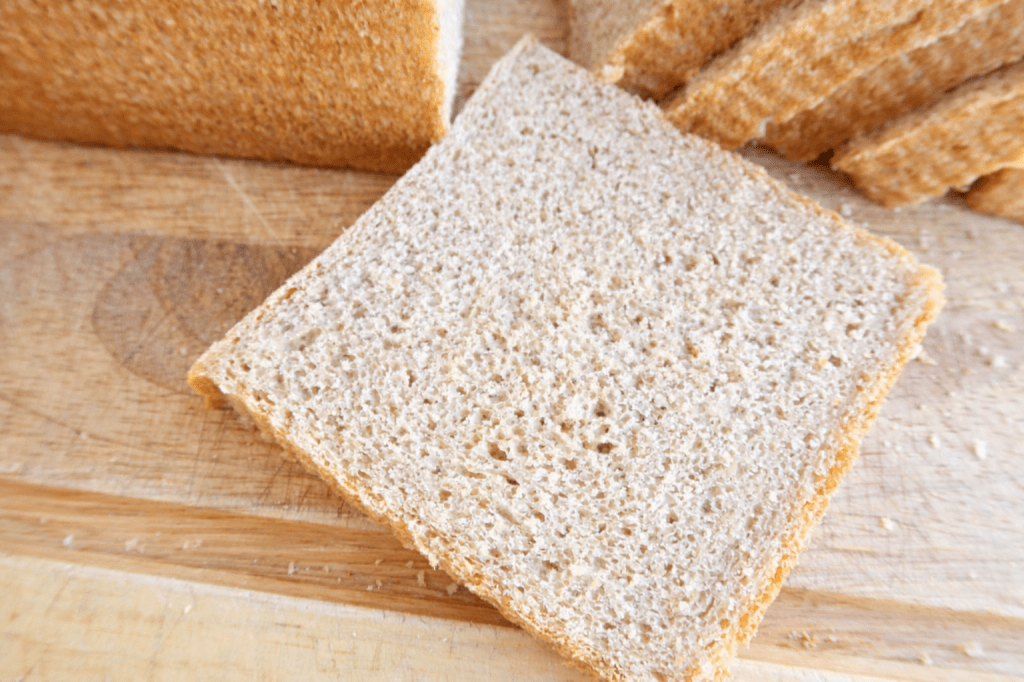 Close-up of a slice of whole grain bread on a wooden cutting board.
