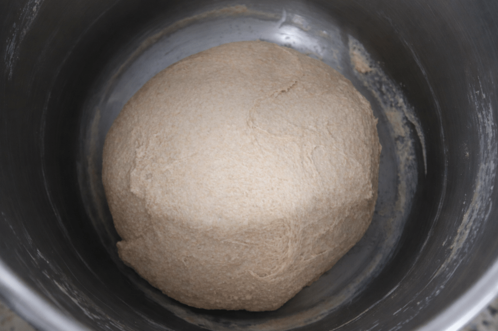 A round ball of dough in a stainless steel mixing bowl.