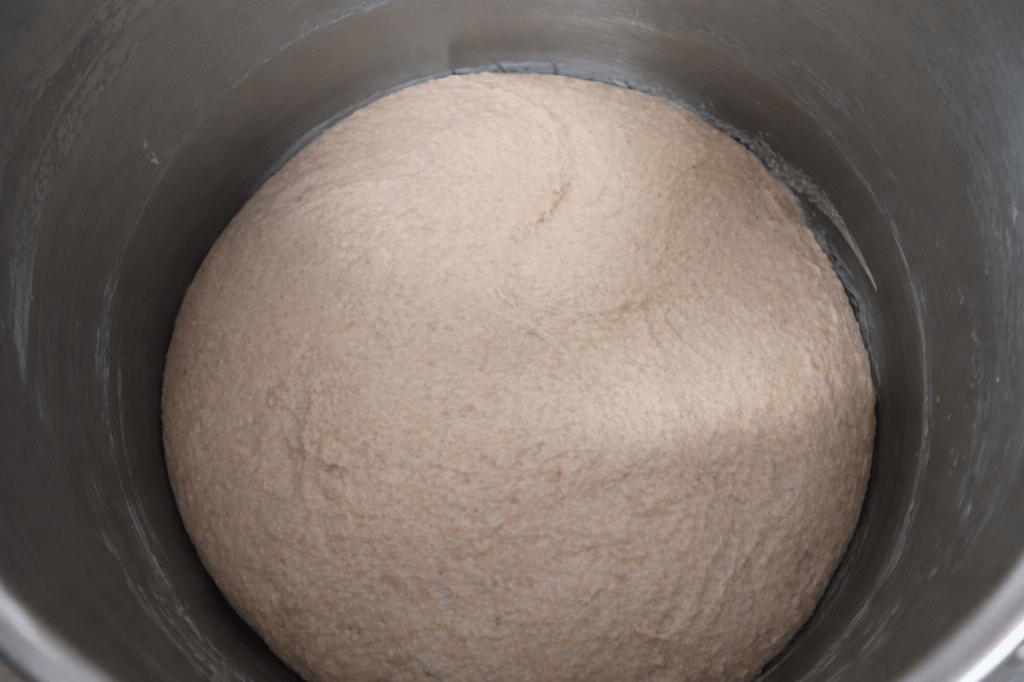 A close-up of risen dough in a metal mixing bowl.