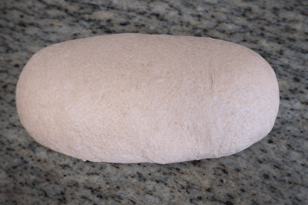 A smooth, oval-shaped piece of raw dough on a granite countertop.