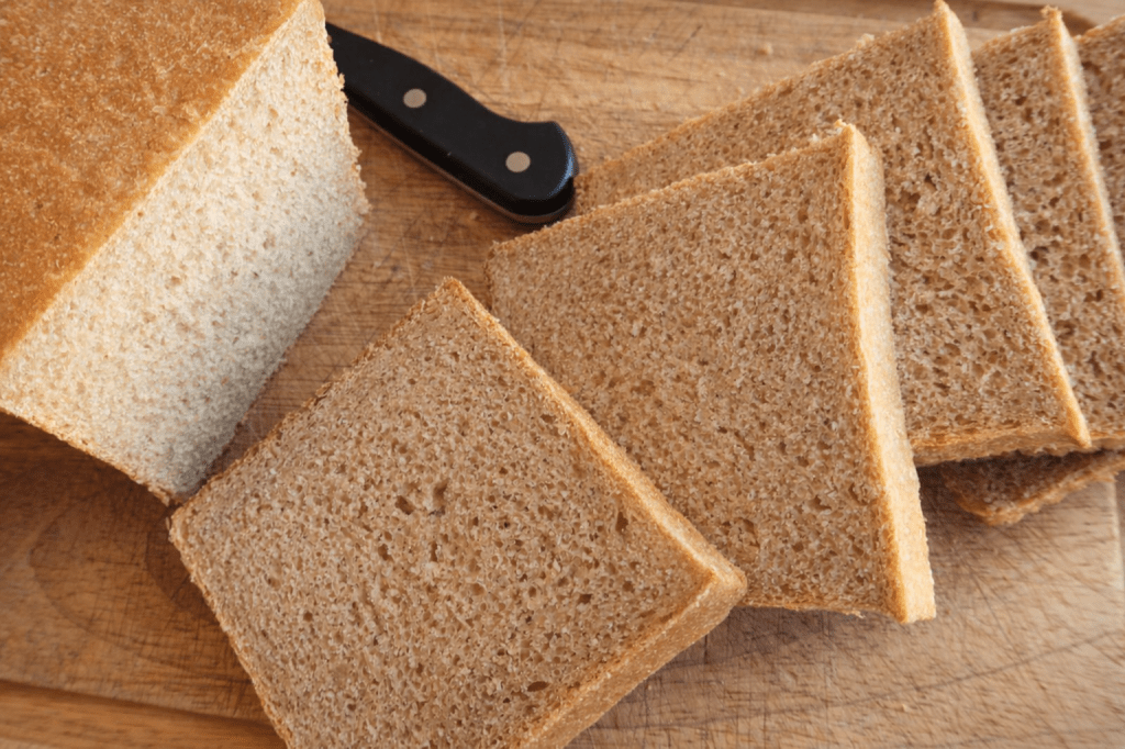 Sliced whole grain bread on a wooden cutting board with a black knife.