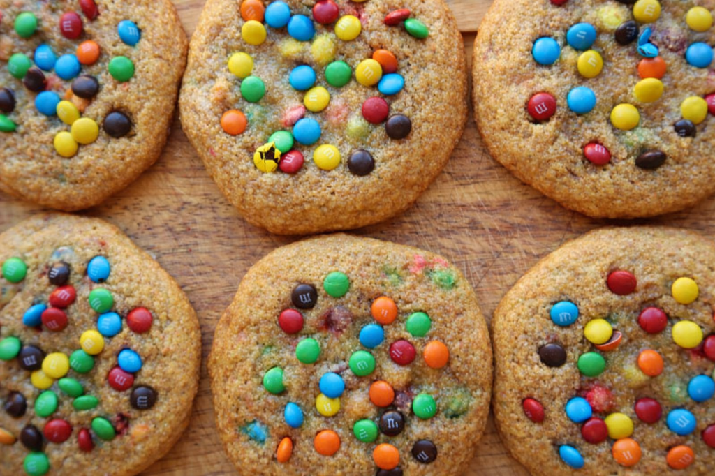 A close-up view of freshly baked cookies topped with colorful chocolate candies on a wooden surface.