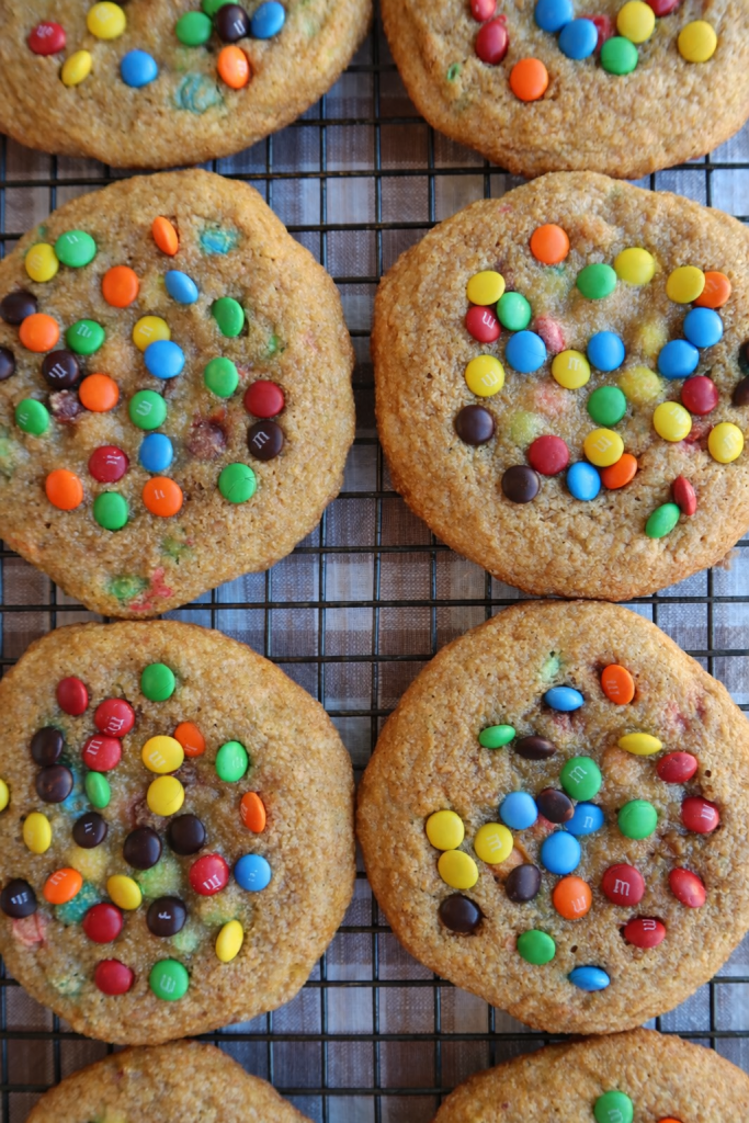 Freshly baked cookies topped with colorful candy-coated chocolates arranged on a wire cooling rack.