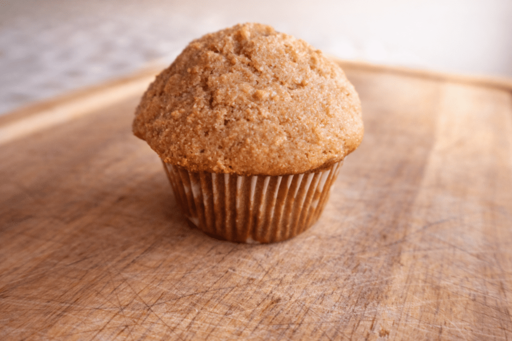 A freshly baked brown muffin sitting on a wooden cutting board.