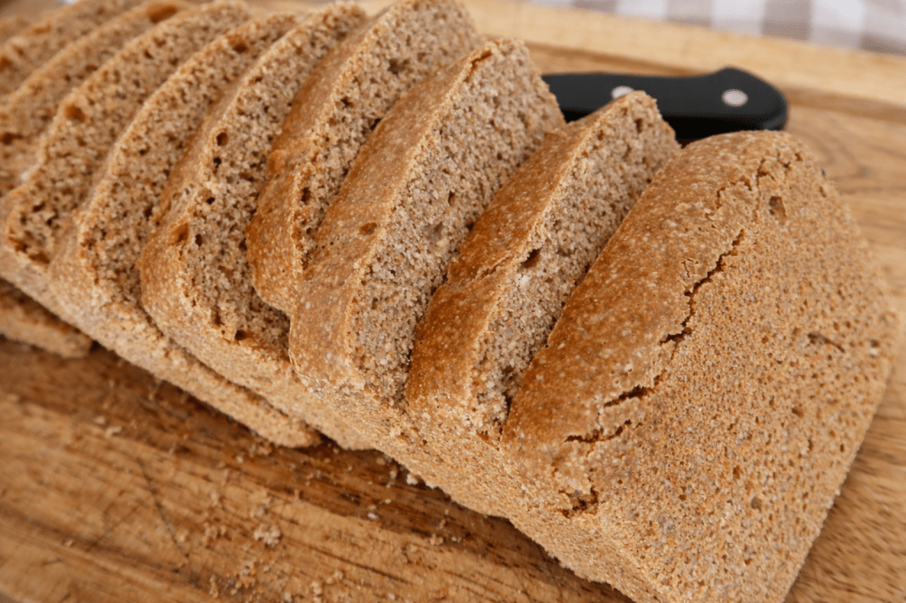 Slices of whole grain bread resting on a wooden cutting board with a knife in the background.