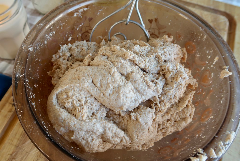 A bowl of thick, unbaked dough with a hand mixer resting inside, surrounded by a kitchen setting.