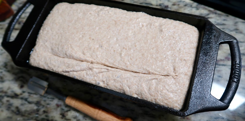 A cast iron loaf pan filled with dough, set on a granite countertop.