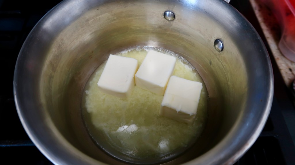 A pot on a stove with three cubes of butter melting in it.
