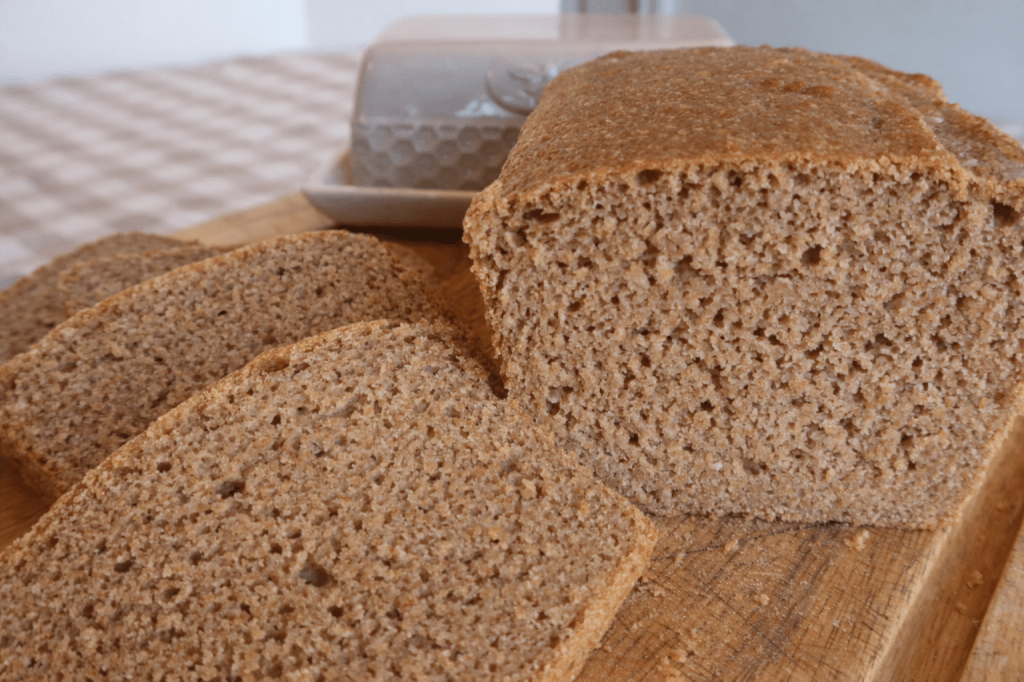 Freshly baked whole grain bread with several slices cut, resting on a wooden cutting board.