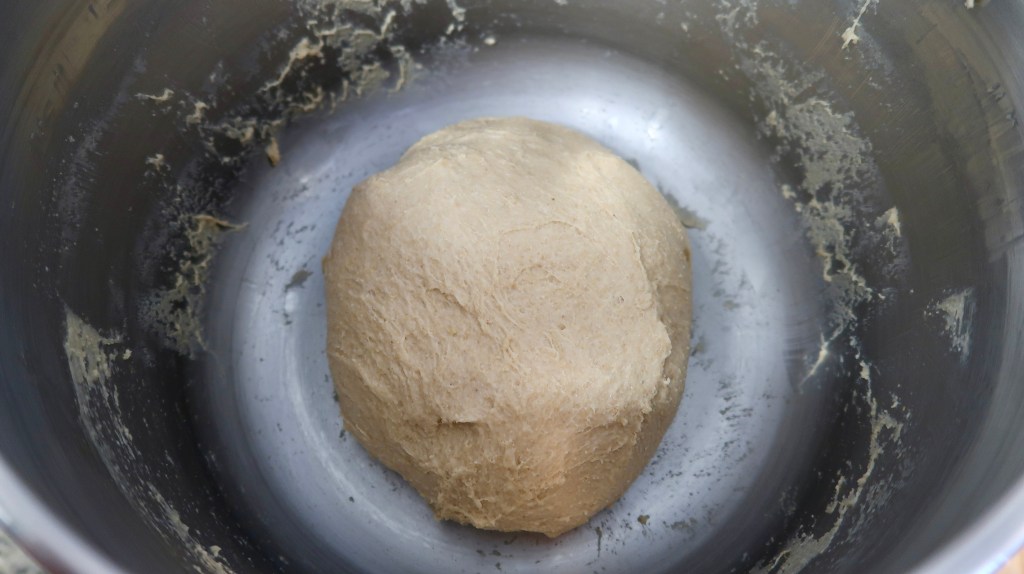 A ball of dough resting in a stainless steel mixing bowl.