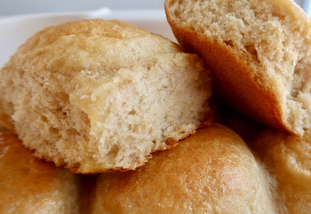 Close-up of fluffy, golden-brown baked bread rolls with a piece broken off to show the soft interior.