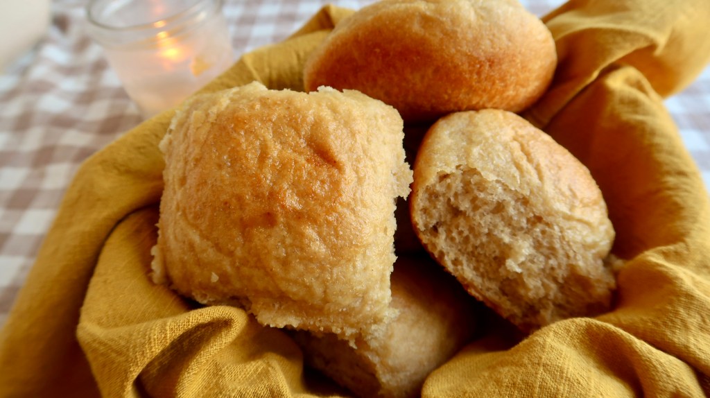 A basket of freshly baked bread rolls resting on a yellow cloth.