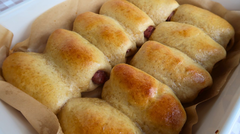 Freshly baked sausage rolls resting on parchment paper, golden brown and fluffy.