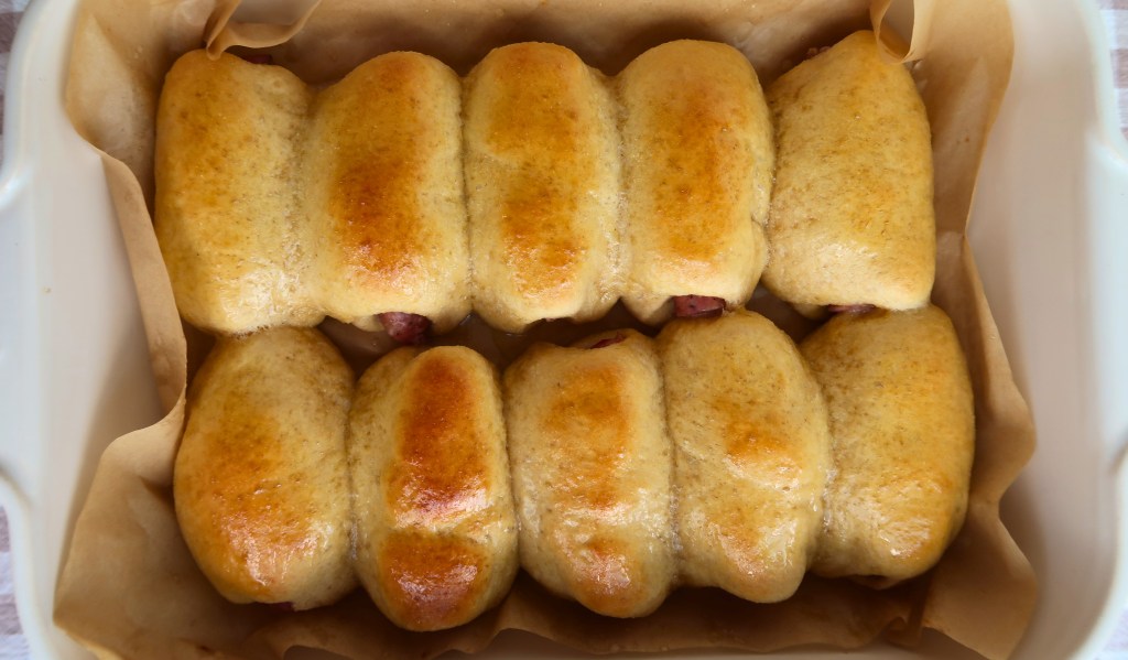 Freshly baked golden-brown rolls arranged in a baking dish lined with parchment paper.
