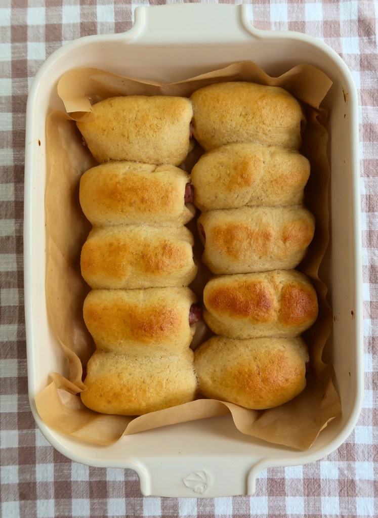 Freshly baked rolls arranged in a white dish lined with parchment paper, set on a checkered tablecloth.