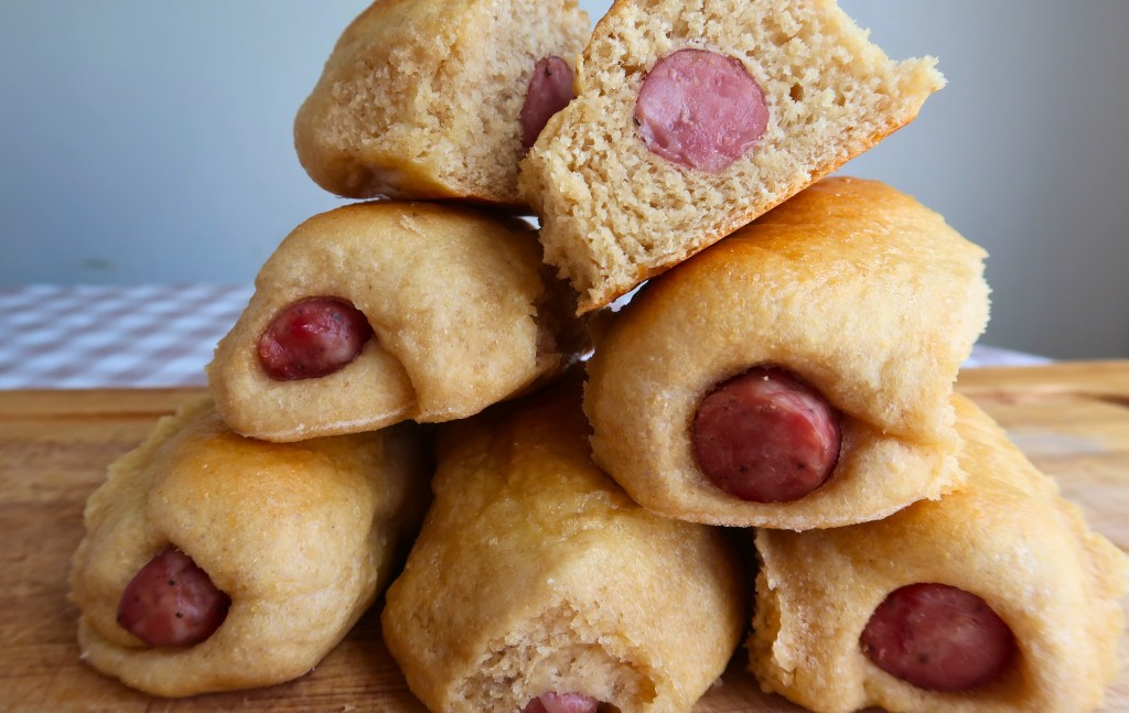 A stack of baked kolaches filled with sausage, with one roll cut in half to show the sausage inside.