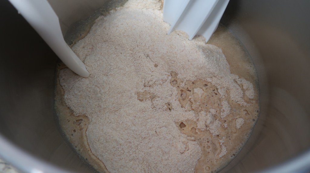 Close-up of a mixing bowl containing flour and yeast mixture with a mixing blade.