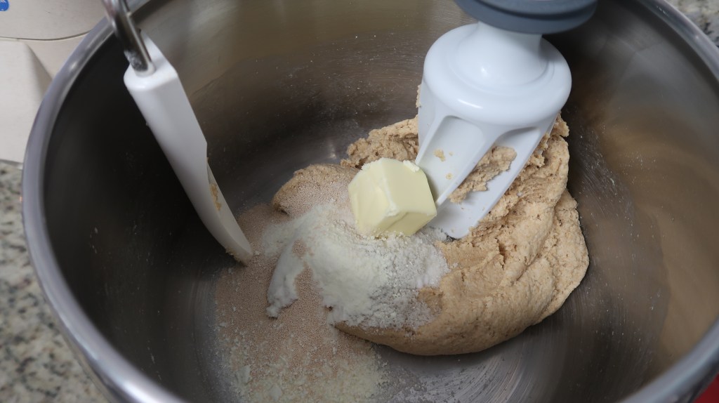 Bowl of dough with butter and flour being mixed by a stand mixer.