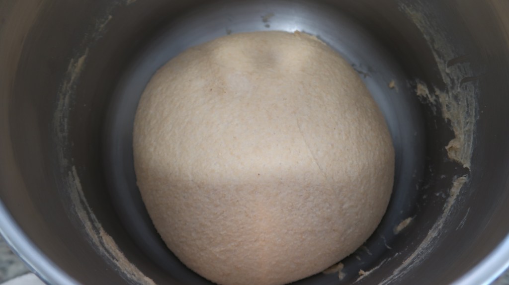 A smooth ball of dough resting in a stainless steel mixing bowl.