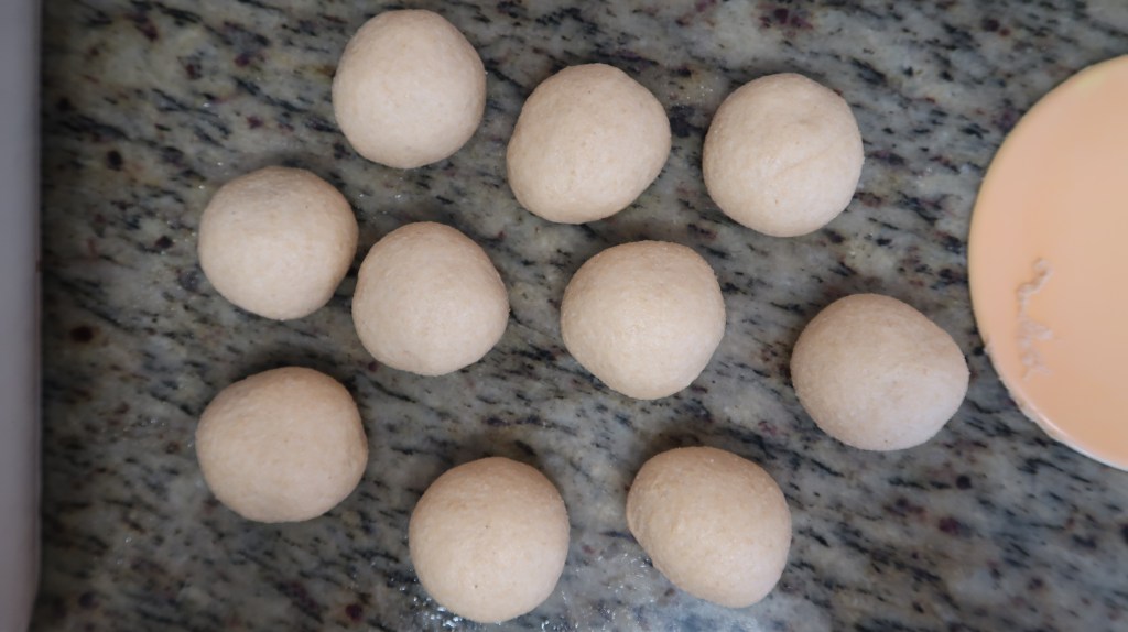 A flat lay of ten small, round dough balls placed on a granite countertop.